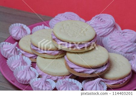 Cooked marshmallow sandwiches. They lie on plate. Next on the plate is a marshmallow of various sizes. 114403201