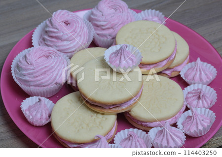 Cooked marshmallow sandwiches. They lie on plate. Next on the plate is a marshmallow of various sizes. 114403250