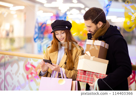 Young caucasian couple with smartphone in shopping mall Young caucasian couple with smartphone in shopping mall 114403366