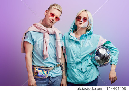 Young fashionable couple of dancers posing with disco ball on violet background Young fashionable couple of dancers posing with disco ball on violet background 114403408