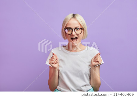 Surprised woman clenches fists with delight, opens mouth widely poses on violet Surprised woman clenches fists with delight, opens mouth widely poses on violet 114403409