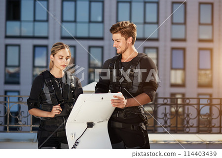 positive male coach showing the working of EMS device to a fit pretty girl positive male coach showing the working of EMS device to a fit pretty girl 114403439