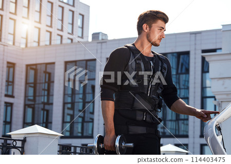 good looking fit man standing with dumbbell on the street 114403475