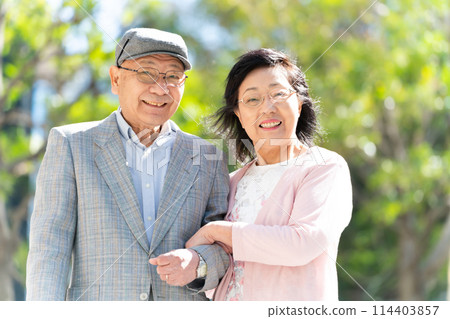 Senior couple walking with walking sticks, green 114403857