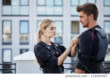 fair-haired awesome girl helping a guy to wear an EMS suit fair-haired awesome girl helping a guy to wear an EMS suit 114404495