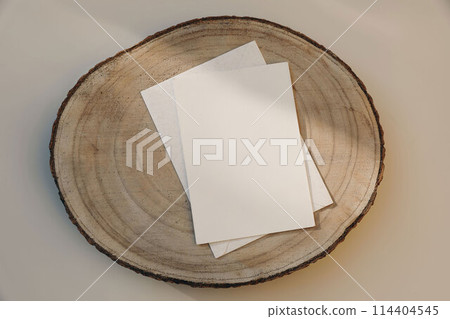 Neutral stationery still life. Blank paper greeting card, invitation mockup with envelope on cut wooden round board. Beige table background in sunlight. Flatlay, top view. No people. 114404545
