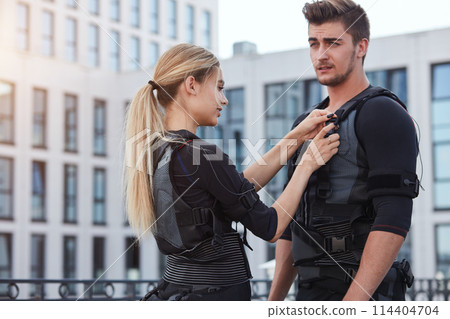 attractive girl is helping her boyfriend to wear an ems costume attractive girl is helping her boyfriend to wear an ems costume 114404704