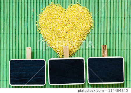 Millet groats heart shaped on green mat surface. 114404840