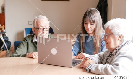 Happy granddaughter teaching senior people to use laptop at nursing home 114405031