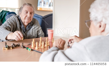 Senior woman playing chess with friend at table in nursing home Senior woman playing chess with friend at table in nursing home 114405058