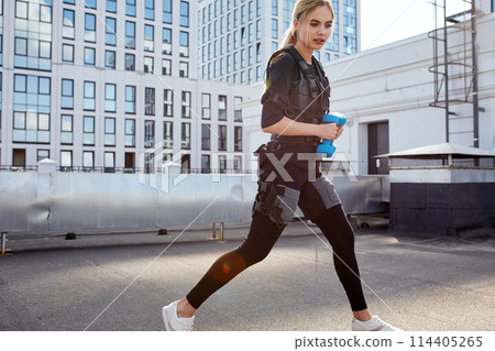 blond girl is jogging with dumbbells and electrical muscule stimulation blond girl is jogging with dumbbells and electrical muscule stimulation 114405265