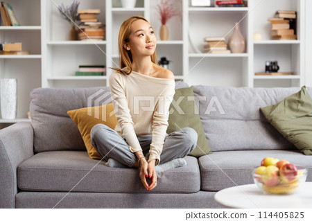 Serene Young Woman Relaxing On Sofa In Modern Living Room Serene Young Woman Relaxing On Sofa In Modern Living Room 114405825