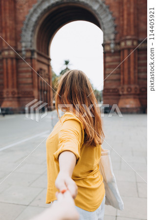 Woman with bag holding man by hand and going to Barcelona triumphal arch. Follow me, Young beautiful woman pulls the arm of her boyfriend in a city park 114405921