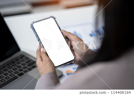 Business - technology and office concept - Hand holding mobile phone with blank screen in office. Business - technology and office concept - Hand holding mobile phone with blank screen in office. 114406184