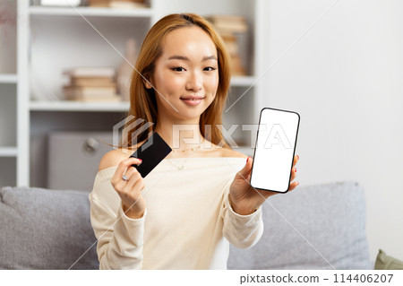 Young Asian Woman Showing Credit Card and Smartphone Indoors Young Asian Woman Showing Credit Card and Smartphone Indoors 114406207