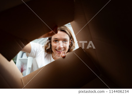 Young Man Smiling While Unpacking Cardboard Box At Home 114406234