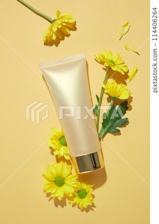 Top view photo at a blank label cosmetic tube in white color featured on yellow background with calendula flower decorated around. Blank space for adding  text or elements of design 114406264