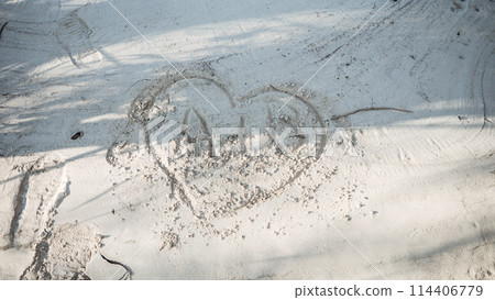 A heart with initials inside is drawn on the white sand of the sea beach. Happy vacation on the sea coast with white soft sand. Drawing on white sand. A heart with initials inside is drawn on the white sand of the sea beach. Happy vacation on the sea coast with white soft sand. Drawing on white sand. 114406779