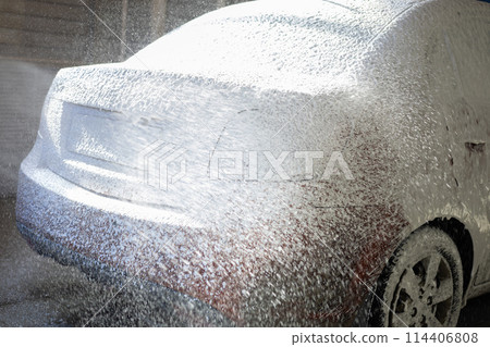 A driver pours foam from a sprayer at a car wash. Dirty orange car covered with foam. A man at a self-service car wash. A driver pours foam from a sprayer at a car wash. Dirty orange car covered with foam. A man at a self-service car wash. 114406808