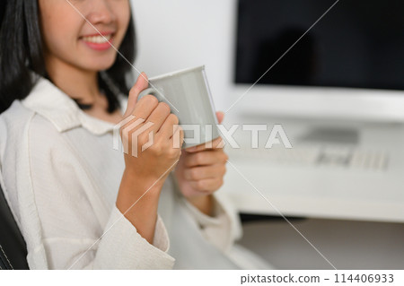 Smiling young businesswoman drinking coffee at the desk in the office Smiling young businesswoman drinking coffee at the desk in the office 114406933