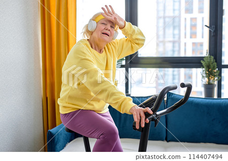 exhausted elderly person training on stationary bicycle doing physical exercise and activity 114407494