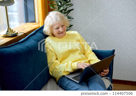 mature retired woman looking at laptop screen, reading news or watching tv series online 114407506