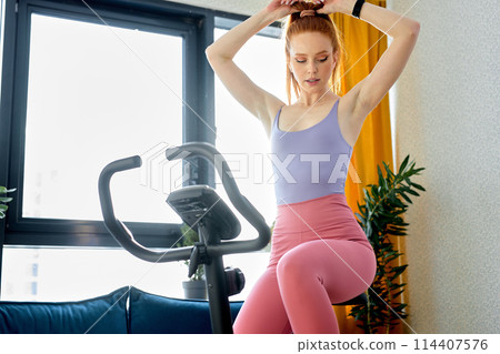 athleye redhead woman working out on exercise bike or stationary bike at home alone 114407576