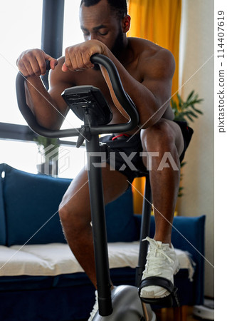 handsome black man working out on exercise bike or stationary bike at home alone 114407619
