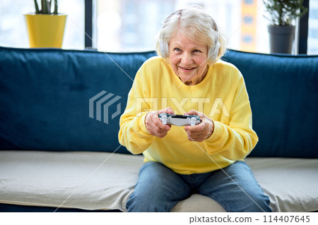 elderly woman enjoying virtual battle, plays video games. Home entertainment concept. 114407645