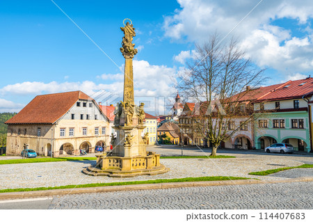 A baroque-style Marian column stands as a centerpiece in Rychorske Square in Zacler, Czech Republic. The square is surrounded by classic European buildings under a bright blue sky. A baroque-style Marian column stands as a centerpiece in Rychorske Square in Zacler, Czech Republic. The square is surrounded by classic European buildings under a bright blue sky. 114407683