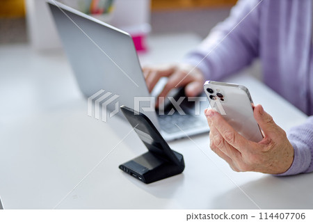 Cropped senior lady checking emails and reading messages on smartphone, at home 114407706