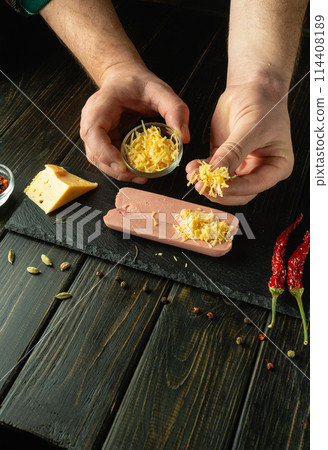 Cooking sausages on the kitchen table by the hands of a cook. Adding cheese to cut raw sausage meat before grilling. Tasty snack serving concept. Cooking sausages on the kitchen table by the hands of a cook. Adding cheese to cut raw sausage meat before grilling. Tasty snack serving concept. 114408189