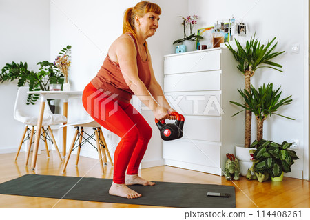 middle-aged woman does yoga in bright spacious room with house plants middle-aged woman does yoga in bright spacious room with house plants 114408261