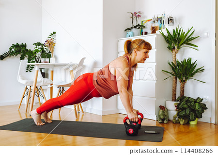middle-aged woman does yoga in bright spacious room with house plants middle-aged woman does yoga in bright spacious room with house plants 114408266