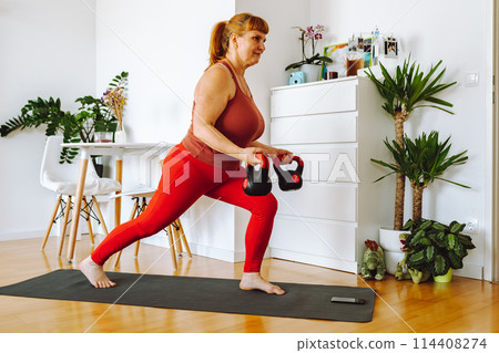 middle-aged woman does yoga in bright spacious room with house plants middle-aged woman does yoga in bright spacious room with house plants 114408274
