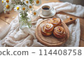 A cinnamon rolls and coffee on table, surrounded by daisies in ceramic vases. 114408758