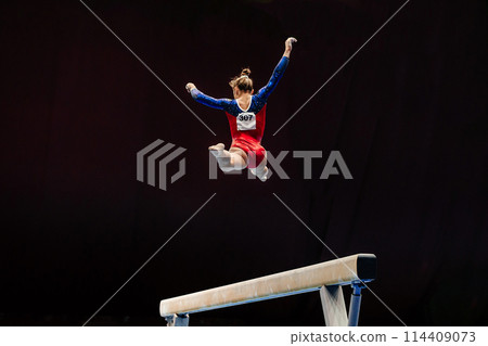 woman exercise on balance beam gymnastics, perform split jump on black background 114409073