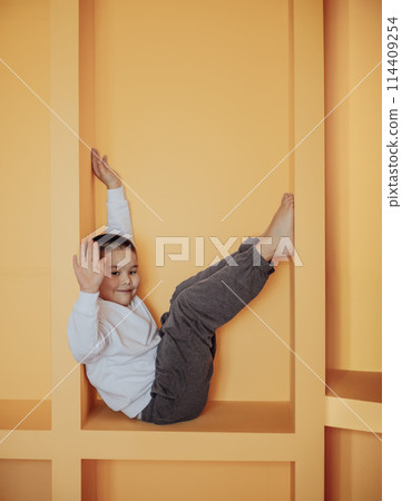 With mischievous grin, boy enjoys his personal hideaway in orange cubby. His pose and surrounding warm colors create lively and inviting atmosphee, perfect for child's imaginative play With mischievous grin, boy enjoys his personal hideaway in orange cubby. His pose and surrounding warm colors create lively and inviting atmosphee, perfect for child's imaginative play 114409254