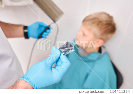 Doctor pointing X-ray unit holding electronic sensor in child. Dentist prepares boy for tooth x-ray image in dental clinic. Doctor pointing X-ray unit holding electronic sensor in child. Dentist prepares boy for tooth x-ray image in dental clinic. 114411254