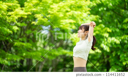 微笑的女人在綠樹中伸展身體 微笑的女人在綠樹中伸展身體 114411652