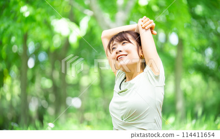 微笑的女人在綠樹中伸展身體 114411654