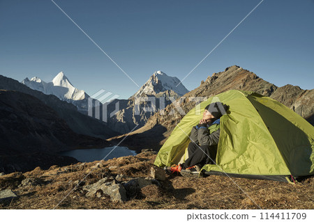 asian woman sitting in tent enjoying early morning sunlight in yading national park, china 114411709