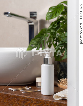 Lotion pump bottle near basin and green plant on wooden countertop in bath, cosmeticmockup 114412677