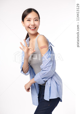 young asian women smiling after getting a vaccine, holding down her shirt sleeve and showing her arm with bandage after receiving vaccination on white background, and she shows ok sign, young asian women smiling after getting a vaccine, holding down her shirt sleeve and showing her arm with bandage after receiving vaccination on white background, and she shows ok sign, 114413129