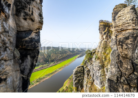 Overlooking the serene Elbe River from the iconic Bastei rock formation in Saxon Switzerland National Park, Germany, on a clear spring day. Overlooking the serene Elbe River from the iconic Bastei rock formation in Saxon Switzerland National Park, Germany, on a clear spring day. 114414670