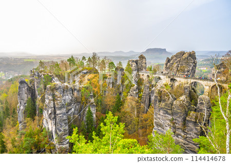 The Bastei Bridge stands tall among majestic sandstone rock formations with visitors enjoying the scenic view at sunset. Kurort Rathen, Saxon Switzerland, Germany The Bastei Bridge stands tall among majestic sandstone rock formations with visitors enjoying the scenic view at sunset. Kurort Rathen, Saxon Switzerland, Germany 114414678