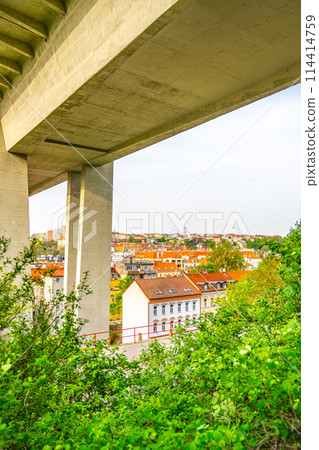 Lush green foliage frames the Nusle Bridge towering over traditional buildings in Prague on a clear spring day. Czechia 114414759