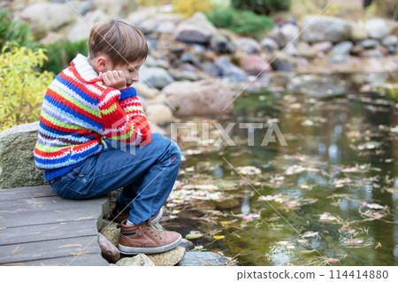 Child on an autumn walk. Sad boy by the lake. 114414880