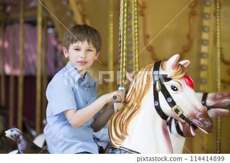 Boy riding a retro carousel in the form of a horse 114414899
