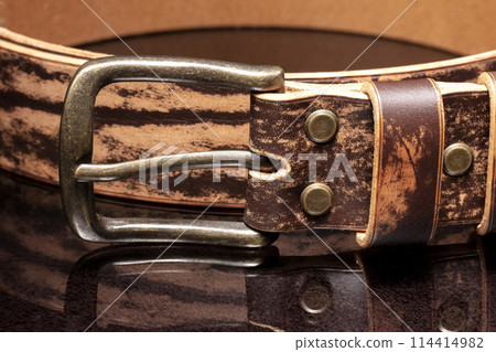 Brown leather belt with scuffs and a metal buckle on a dark background. 114414982